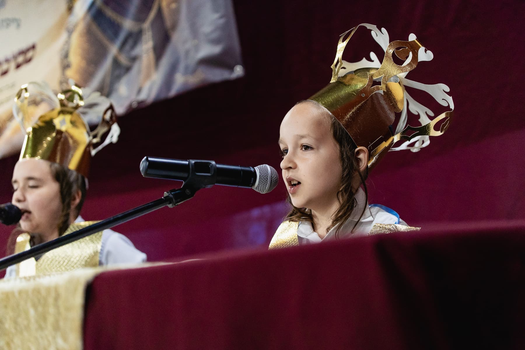 A young boy in a gold crown speaking at the microphone during Mesibat Chumash