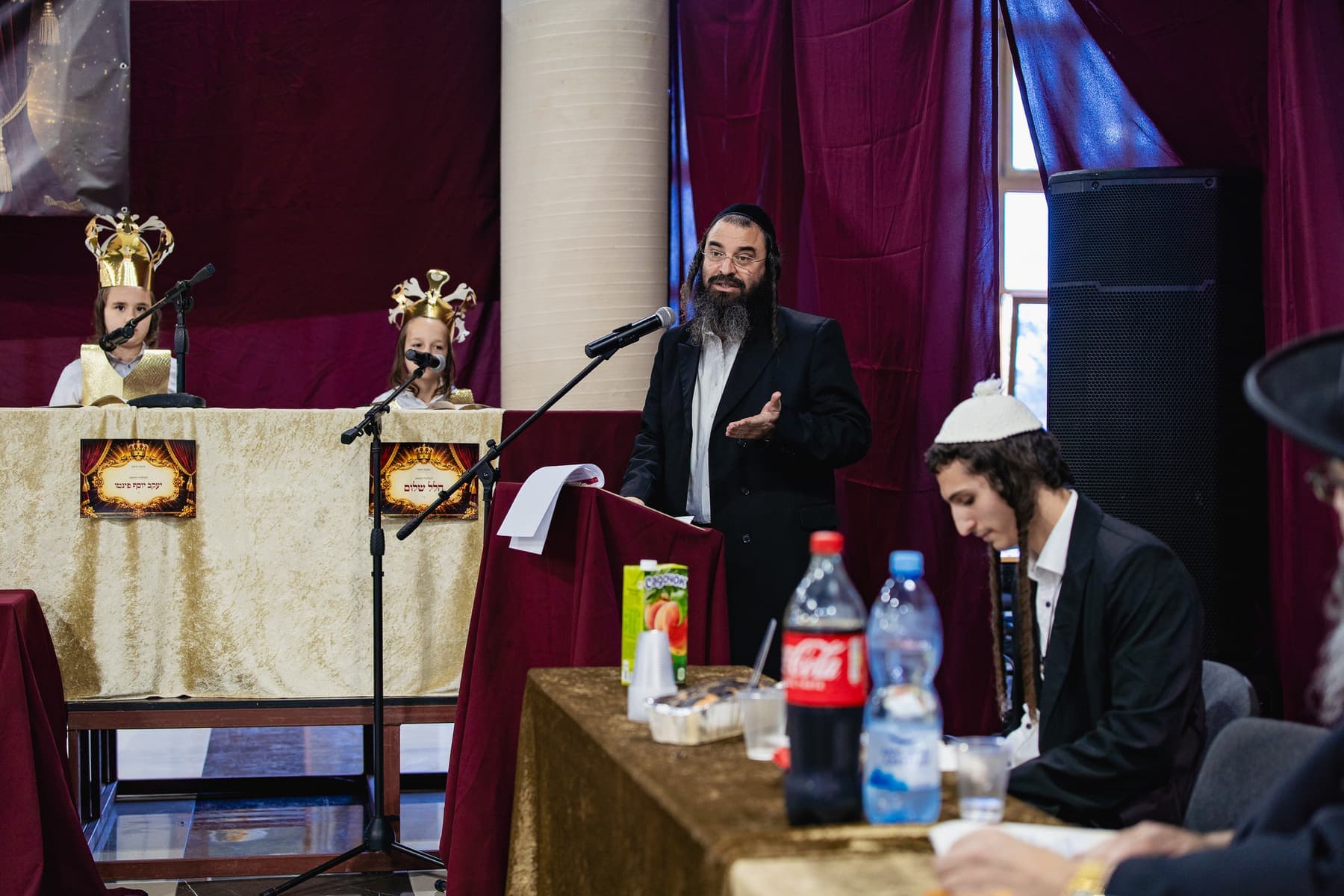 A speaker addressing the Mesibat Chumash gathering with students in gold crowns