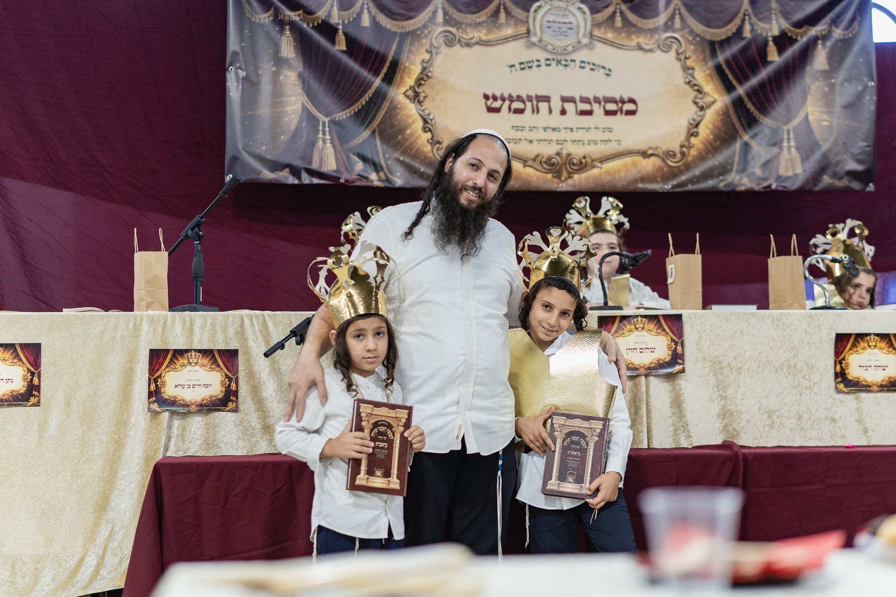 A teacher with two boys in gold crowns holding their new Chumashim